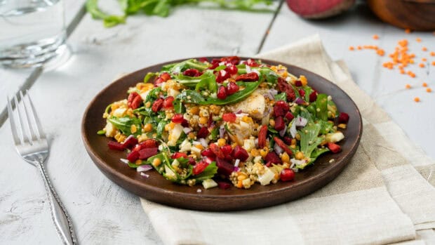 A plate of fresh quinoa salad with spinach, pomegranate, and various vegetables on a wooden table, 2K Desktop Wallpaper