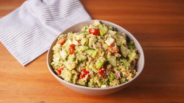 A bowl of quinoa salad with cucumbers, cherry tomatoes, and herbs on a wooden table, HD Desktop Wallpaper