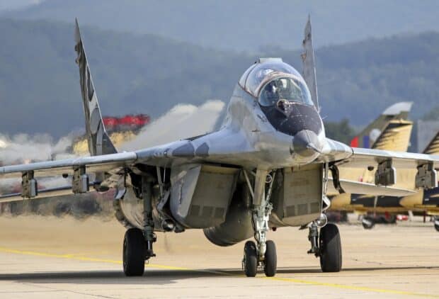 A sleek military jet fighter taxis on the runway with mountains in the background, HD Desktop Wallpaper