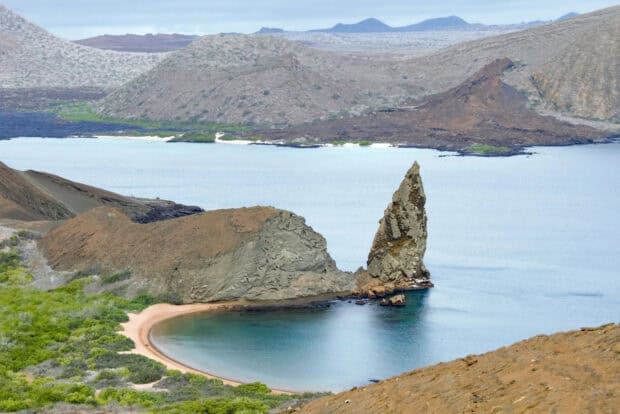 A sharp rock formation stands tall by the calm bay at Galapagos Islands, HD Desktop Wallpaper