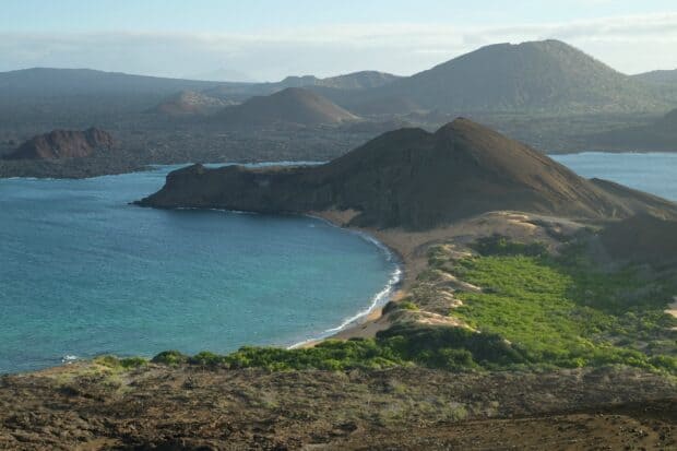 A scenic view of the Galapagos Islands volcanic coastline with blue ocean and green vegetation, 2K Desktop Wallpaper