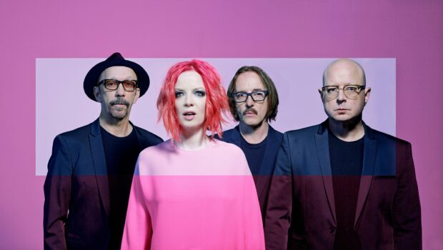 Garbage band members stand against a pink background wearing dark blazers and colorful outfits, HD Desktop Wallpaper