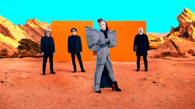The Garbage Band stands in a colorful desert landscape with styled costumes and bright orange panels behind, HD Desktop Wallpaper