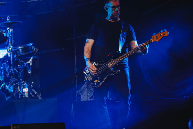A musician from the Garbage Band is playing bass guitar on stage during a live performance, 2K Desktop Wallpaper