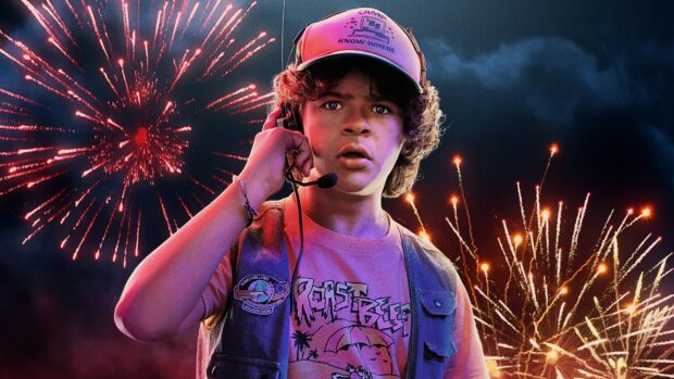 Gaten Matarazzo stands wearing a headset and colorful vest with fireworks in the background, 4K Desktop Wallpaper