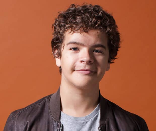 A close up portrait of Gaten Matarazzo smiling against an orange background, HD Mobile Wallpaper