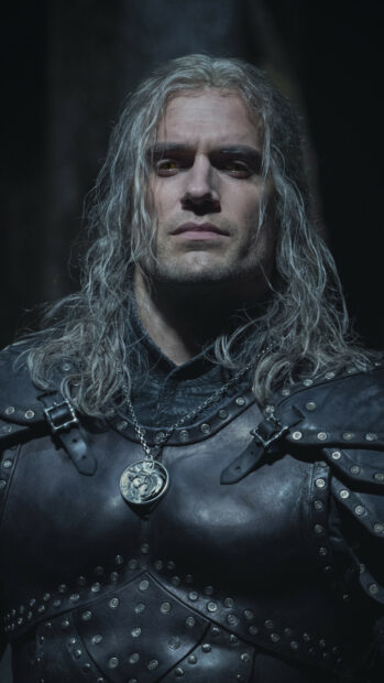 Geralt of Rivia stands wearing dark armor and a wolf medallion in The Witcher Tv Series, 2K Mobile Wallpaper