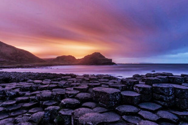 The Giants Causeway is shown with purple rocks and a dramatic colorful sunset sky, 2K Desktop Wallpaper