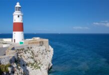 A Gibraltar lighthouse stands tall on rocky cliffs overlooking the deep blue sea, 2K Desktop Wallpaper
