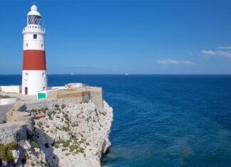 A Gibraltar lighthouse stands tall on rocky cliffs overlooking the deep blue sea, 2K Desktop Wallpaper