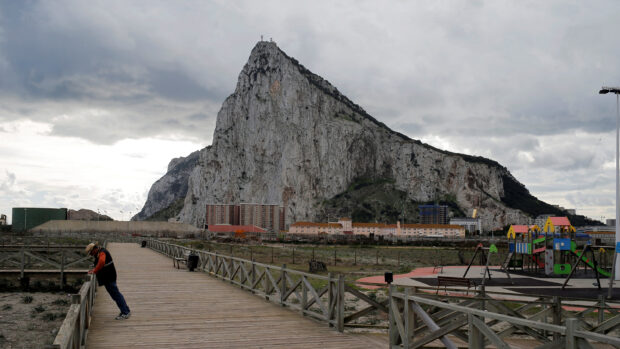 A man leans on a wooden fence near Gibraltar rock under cloudy skies, 2K Desktop Wallpaper