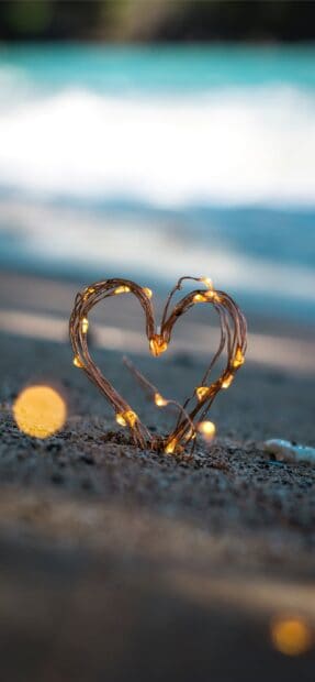 A glowing heart shape made of string lights on sandy beach at dusk, 2K Mobile Wallpaper