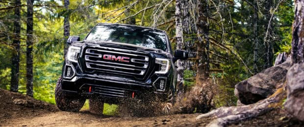 A GMC Sierra drives through a forest trail kicking up dirt and mud, 2K Desktop Wallpaper