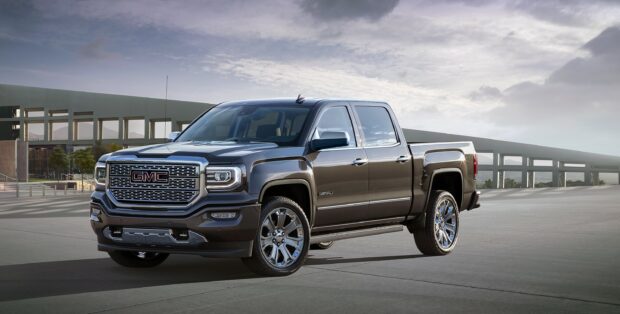 A Gmc Sierra truck is parked in front of a modern building under a partly cloudy sky, 2K Desktop Wallpaper