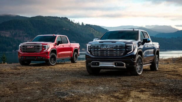 Two GMC Sierra trucks are parked on dry ground near a lake with mountains in the background, HD Desktop Wallpaper