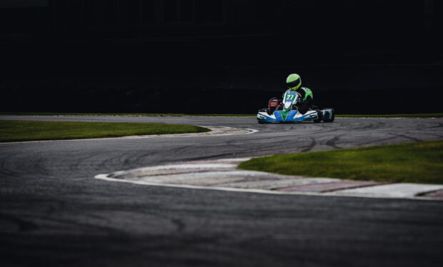 A go kart driver wearing a green helmet races on a curved race track, 2K Desktop Wallpaper