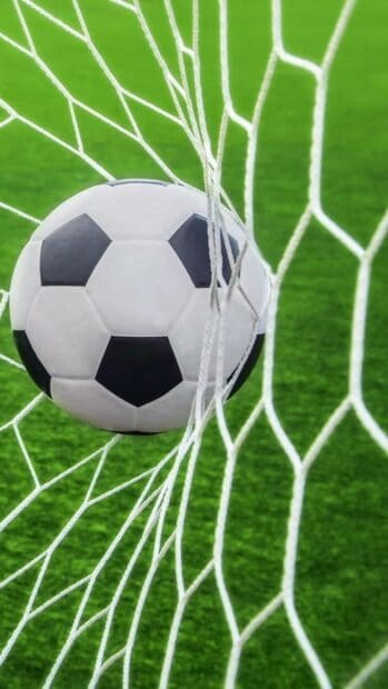 A soccer ball is caught in the net after a goal during a football match with green grass, 2K Phone Wallpaper