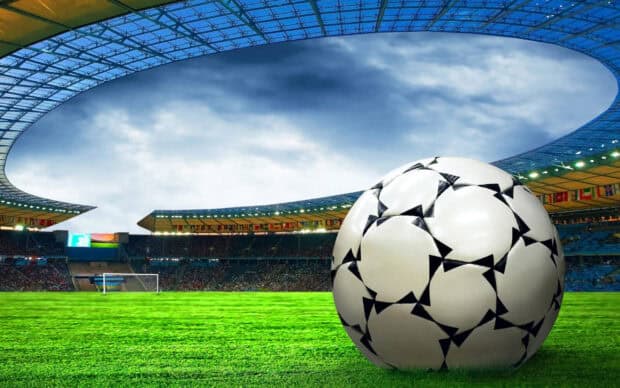 A classic black and white soccer ball sits on the vibrant green grass of a large stadium, 2K Desktop Wallpaper