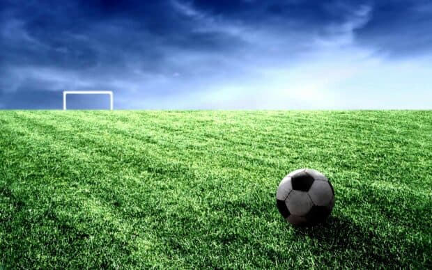 A soccer ball lies on green grass in front of a goal with clear sky, 2K Desktop Wallpaper