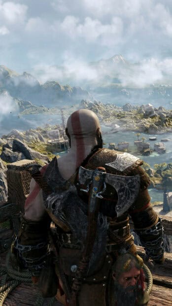 A warrior from God of War Ragnarok stands on a cliff edge overlooking a vast mountainous landscape, 4K Phone Wallpaper