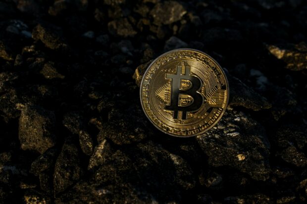 A gold bitcoin coin is resting on dark textured rocks in close up view, 2K Desktop Wallpaper