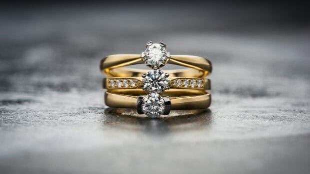 A close up of gold rings featuring sparkling diamonds stacked on a grey textured surface with blurred background, HD Desktop Wallpaper