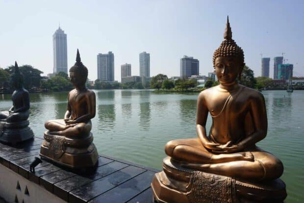 Bronze Buddha statues peacefully sitting near the water with Colombo cityscape in the background, HD Desktop Wallpaper