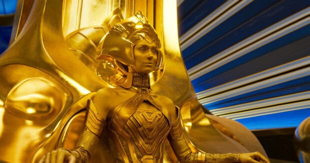 Elizabeth Debicki wears an intricate golden armor suit seated on a metallic throne, HD Desktop Wallpaper