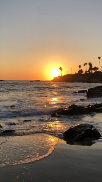The Laguna Beach displays a golden sunset over the ocean with waves touching the rocky shore, HD Phone Wallpaper
