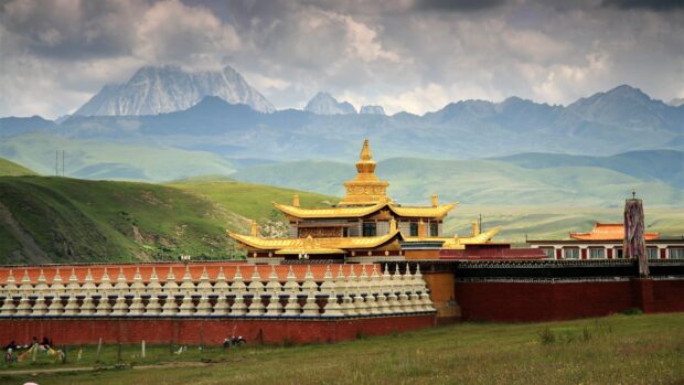 A golden Tibetan temple stands with the majestic Himalayan mountains in the background, surrounded by green hills, 4K Desktop Wallpaper