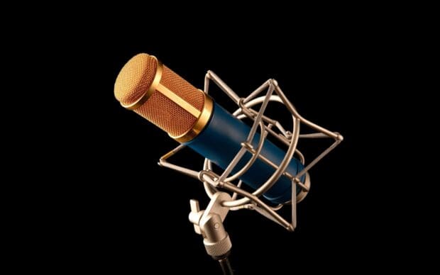 A golden and blue microphone is secured in a silver shock mount against a black background, 2K Desktop Wallpaper