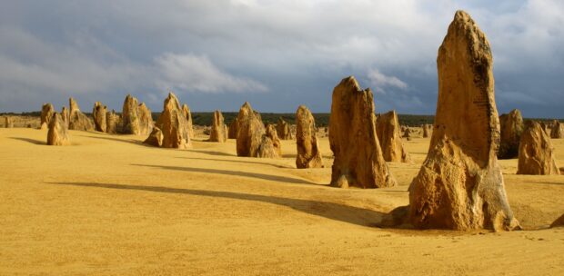 Tall limestone pillars stand over yellow sandy ground under a cloudy sky at Nambung National Park, 2K Desktop Wallpaper