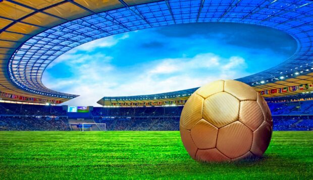 A golden soccer ball rests on the grass near the goalpost in a large stadium filled with spectators, 2K Desktop Wallpaper
