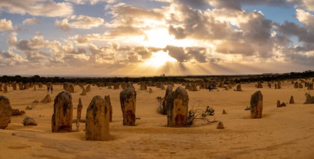 The Nambung National Park desert landscape features limestone pillars under golden sunlight beams. 2K Desktop Wallpaper