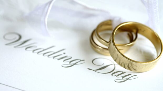 Two golden wedding rings resting on a white wedding invitation with elegant script text, HD Desktop Wallpaper