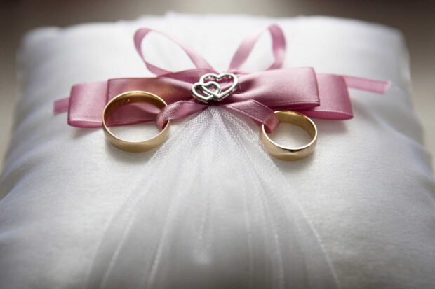Two golden wedding rings lie on white fabric tied with a pink ribbon and a silver heart ornament, HD Desktop Wallpaper
