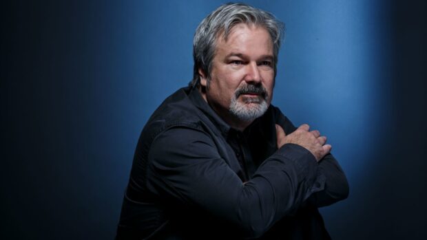 Gore Verbinski looks thoughtful with arms crossed in front of a blue background, HD Desktop Wallpaper