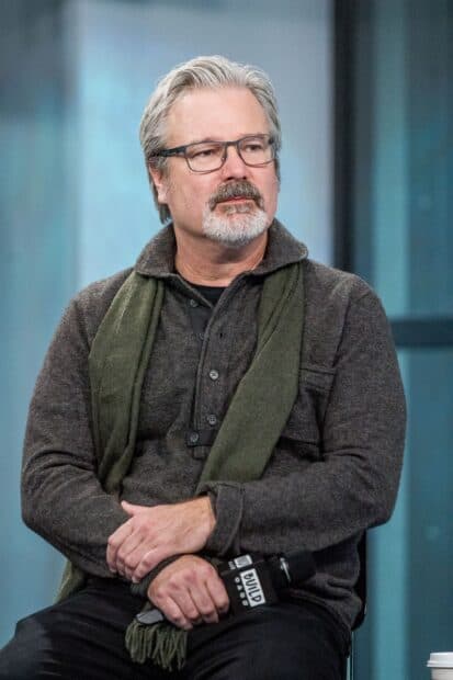 Gore Verbinski is sitting with folded hands holding a microphone during an interview, 2K Portrait Mobile Wallpaper