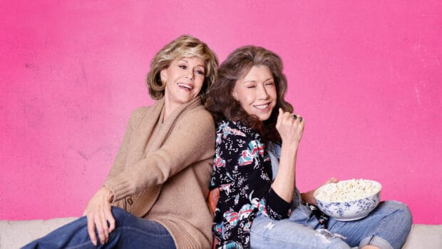 Two women from Grace And Frankie Netflix sit back to back smiling with a bowl of popcorn, HD Desktop Wallpaper