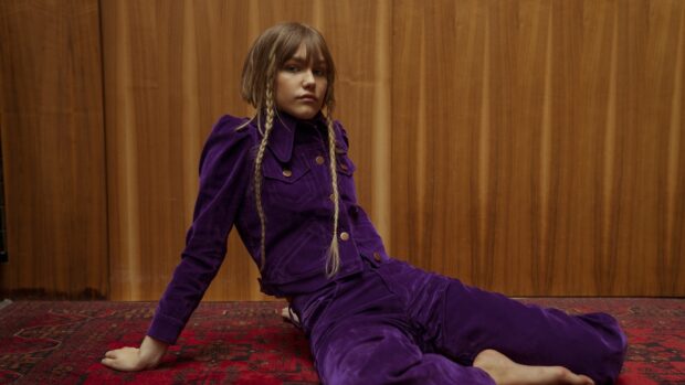 A young woman wearing a purple outfit and sitting on a red rug with wooden panel background featuring Grace Vanderwaal, 4K Desktop Wallpaper