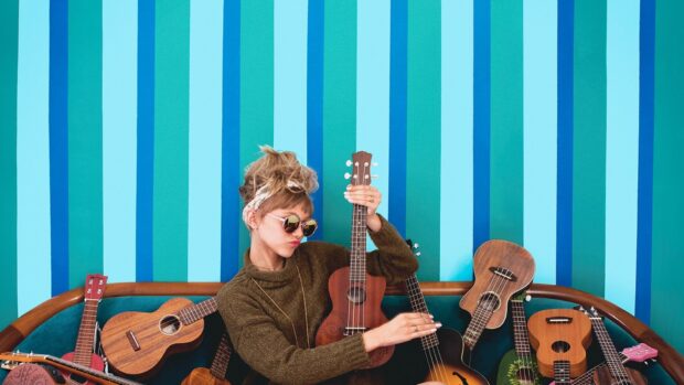 Grace Vanderwaal is playing a ukulele surrounded by multiple ukuleles in a brightly striped room, HD Desktop Wallpaper