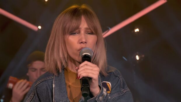Grace Vanderwaal sings into a microphone during a live performance with stage lights around her, 4K Desktop Wallpaper