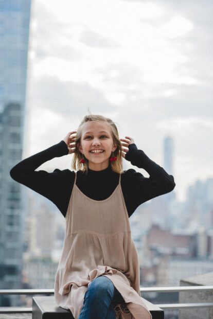 Grace Vanderwaal smiles happily while sitting outside with a cityscape in the background, HD Mobile Wallpaper