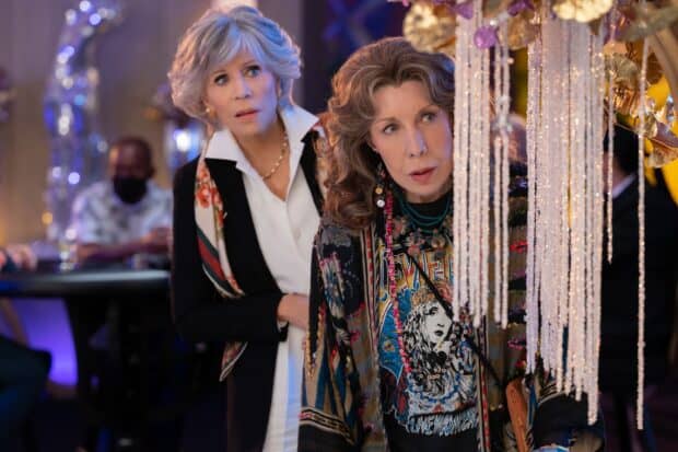 Grace and Frankie are curiously looking at hanging decorations in a vibrant setting, 2K Desktop Wallpaper