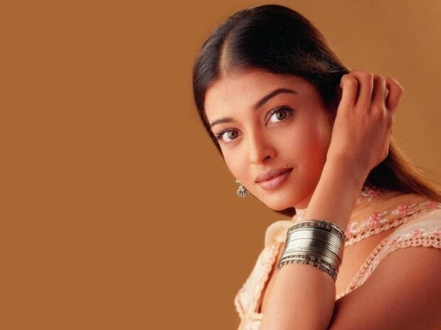 Aishwarya Rai is posing elegantly with silver bangles against a brown background, HD Desktop Wallpaper