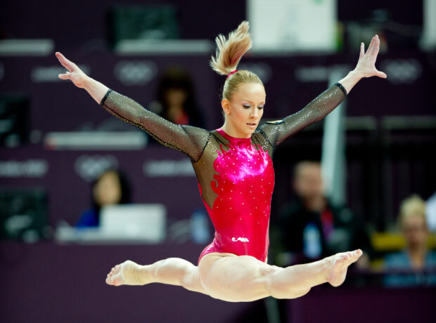 A female acrobatic gymnast performs a split leap in a sparkling red leotard during a competition, 2K Desktop Wallpaper