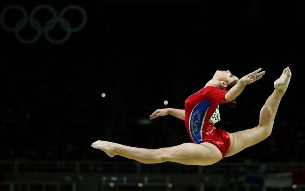 A gymnast performs an elegant leap on the balance beam during a competition, HD Desktop Wallpaper