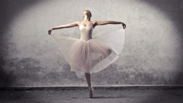 A ballet dancer in a white tutu performs a balanced pose against a textured wall, HD Desktop Wallpaper