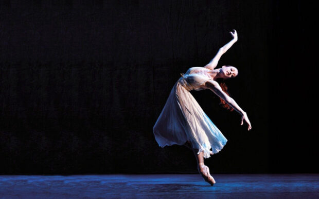 A ballet dancer is captured performing a graceful leap on stage under dramatic lighting, HD Desktop Wallpaper