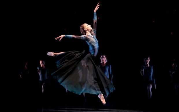A ballet dancer leaps elegantly on stage in a dramatic pose with other dancers behind, HD Desktop Wallpaper